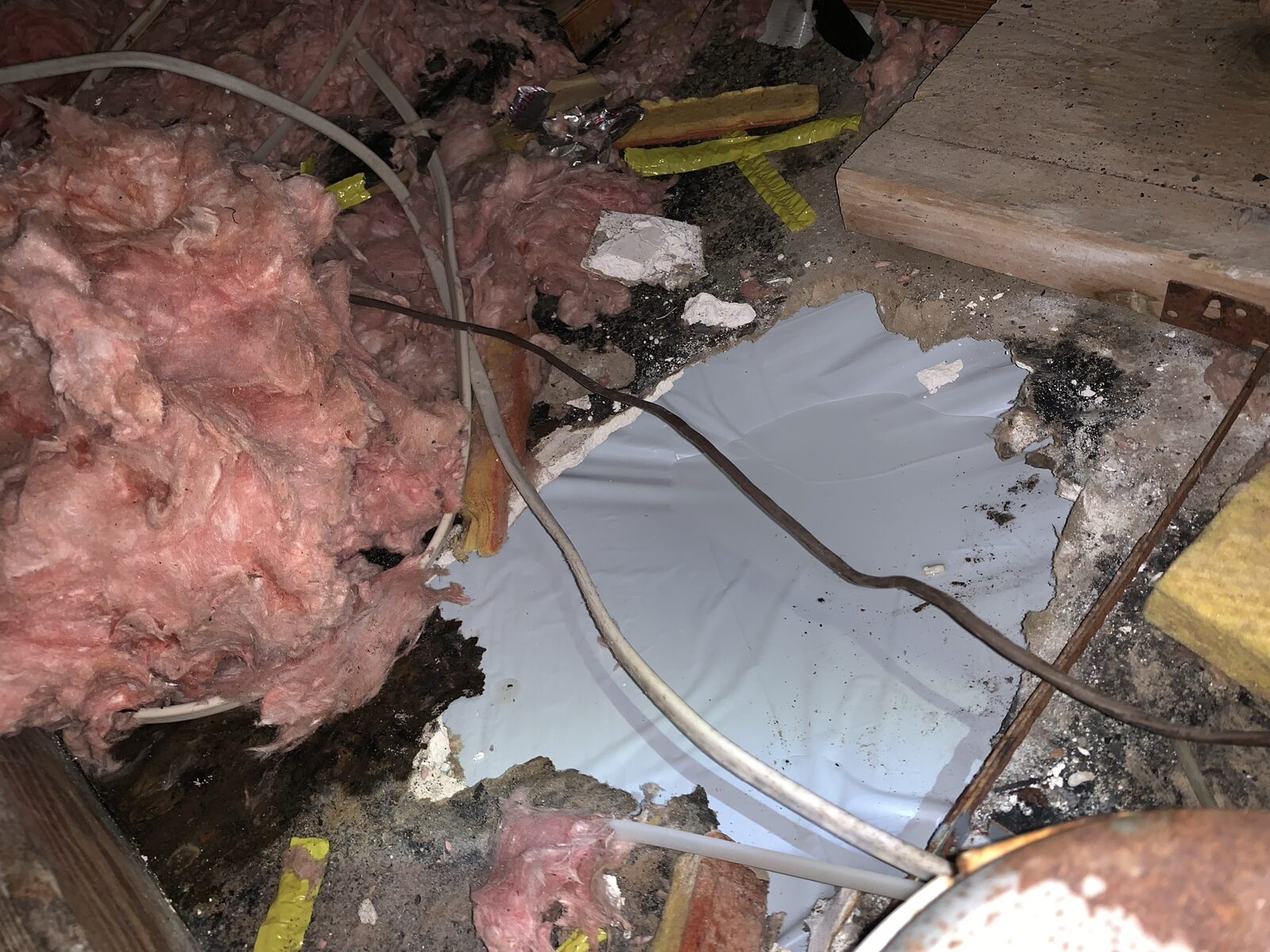 Storm-damaged attic with torn pink fiberglass insulation, debris and a loose refrigerant line